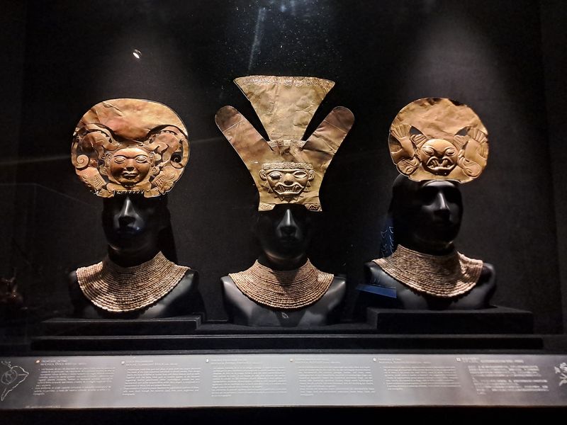 Drei goldene Inka Kronen vor schwarzem Hintergrund in einem Museum.
