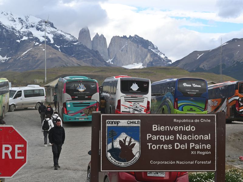 Mehrere Tourbusse, die am Parkeingang gerade Passagiere abgeladen haben. Die Torres-Türme sind dabei im Hintergrund zu sehen.