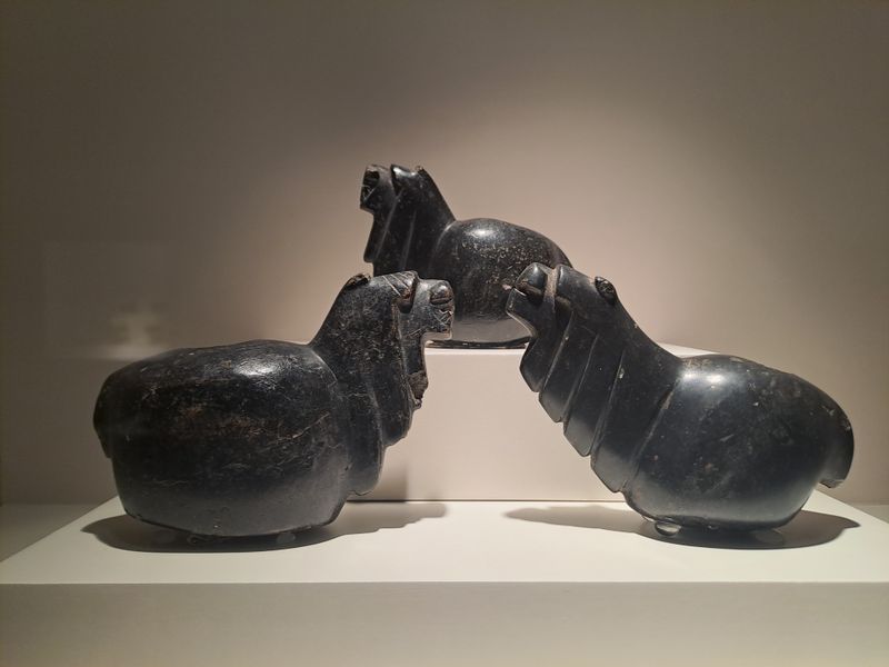 Drei aus dunklem Stein gefertigtem Lamafiguren in einem Museum.