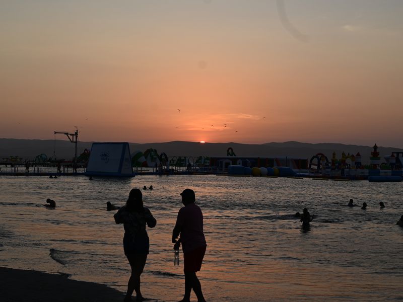 Strand bei Abendsonne, im Hintergrund ist eine schwimmende Kinderhüpfburg zu sehen.