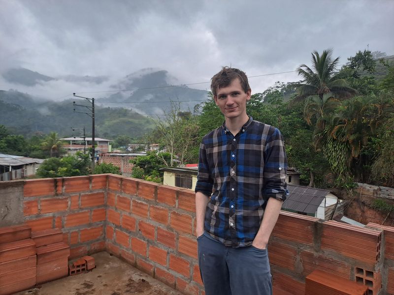 Pascal steht auf dem Dach vom Gasthaus mit Ausblick auf bewaldete Berge.