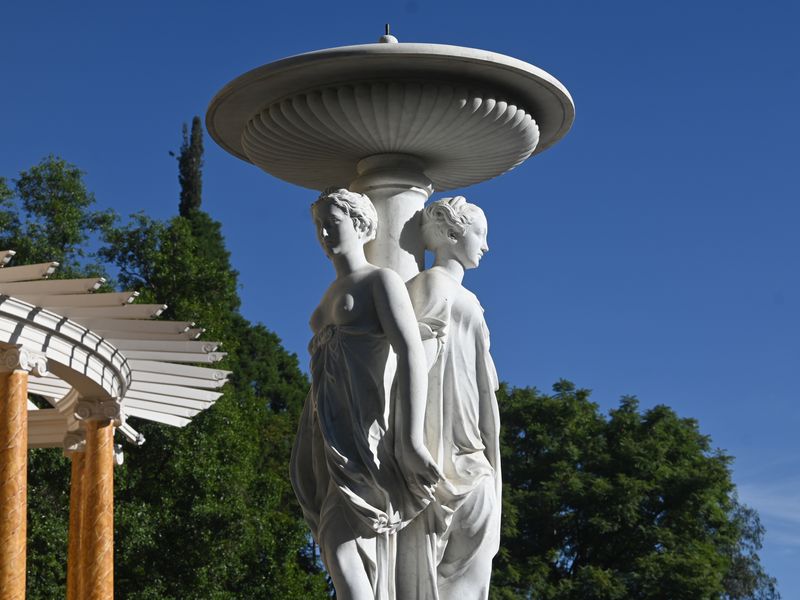 Ein Springbrunnen im Park der von zwei halbnackten marmornen Frauen am Kopf getragen wird.