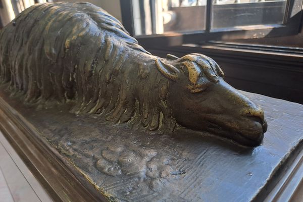 Der Bronzeguss eines Lamas, dass auf dem Boden liegt und schläft.