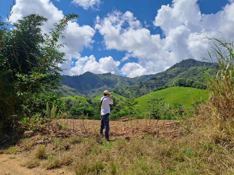Pascal im weißen Hemd, steht im Grün und und macht ein Bild mit der Kamera.