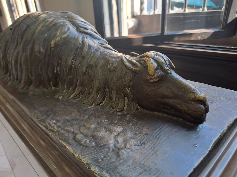 Der Bronzeguss eines Lamas, dass auf dem Boden liegt und schläft.