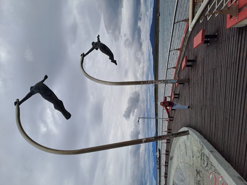 Zwei nackte fliegnde Skulpturen am Wasser.